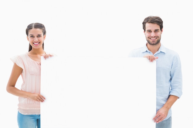 Jovem casal atraente sorrindo na câmera segurando poster