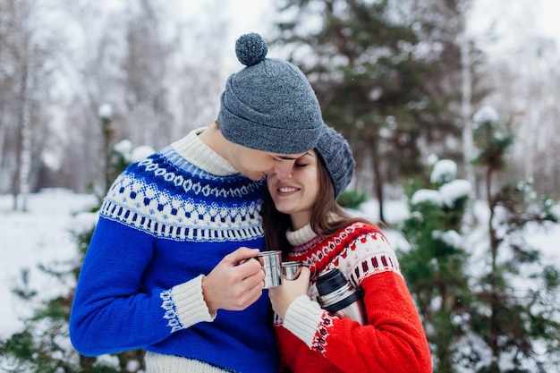 Jovem casal bebendo chá na floresta de inverno Pessoas felizes relaxando ao ar livre durante as férias do dia dos namorados