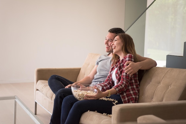 jovem casal bonito aproveitando o tempo livre assistindo televisão com pipoca em sua casa de luxo