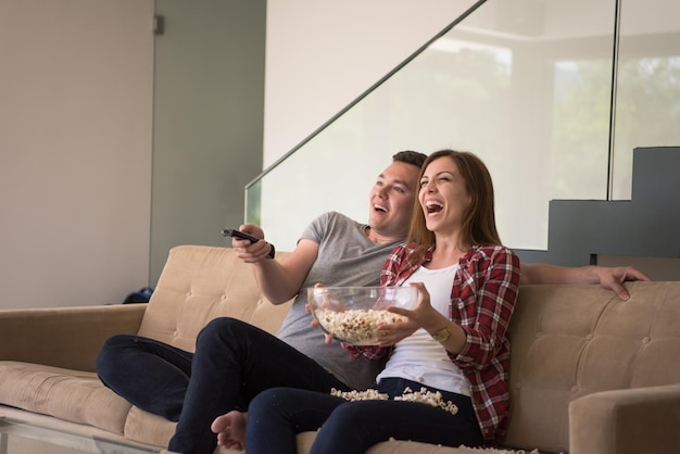 jovem casal bonito aproveitando o tempo livre assistindo televisão com pipoca em sua casa de luxo