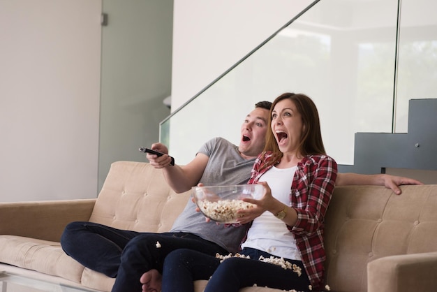 jovem casal bonito aproveitando o tempo livre assistindo televisão com pipoca em sua casa de luxo