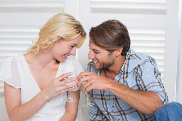 Jovem casal bonito sentado no chão juntos tendo vinho branco