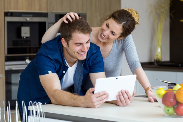 Foto jovem casal bonito usando comprimidos digitais na cozinha em casa.