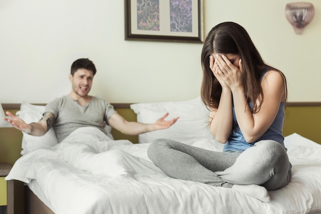 Foto jovem casal brigando e mulher chorando enquanto está sentada na cama em casa