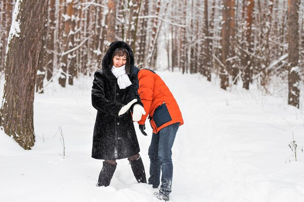 Jovem casal brincando na neve, tendo uma luta de bolas de neve.