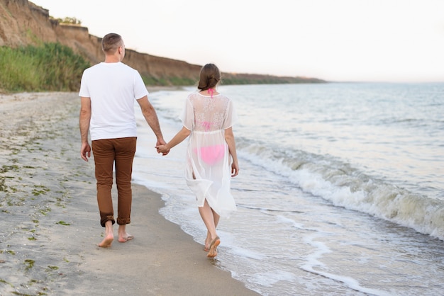 Jovem casal caminha as mãos ao longo da costa do mar. Vista traseira