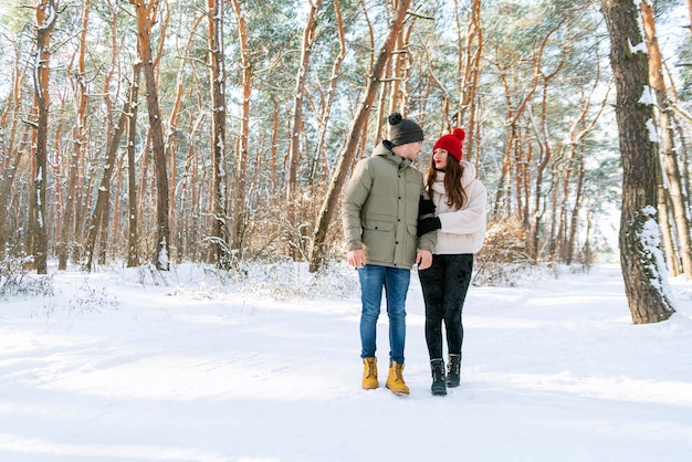 Jovem casal caucasiano apaixonado andando no parque nevado e de mãos dadas. Cara e uma garota estão andando na floresta de inverno nevado.