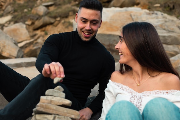 Jovem casal caucasiano construindo uma torre de pedra na praia