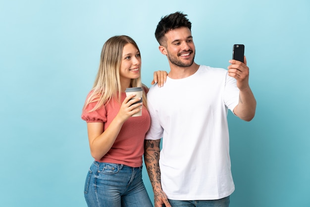 Jovem casal caucasiano em azul fazendo uma selfie com o celular