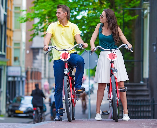 Jovem casal caucasiano feliz em bicicletas nas ruas antigas de Amsterdã