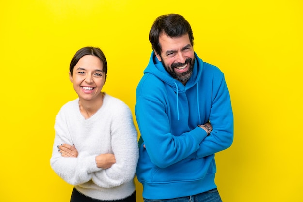 Jovem casal caucasiano isolado em fundo amarelo, mantendo os braços cruzados enquanto sorria