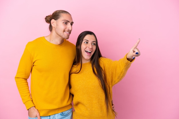 Jovem casal caucasiano isolado em fundo rosa apresentando uma ideia enquanto olha sorrindo para