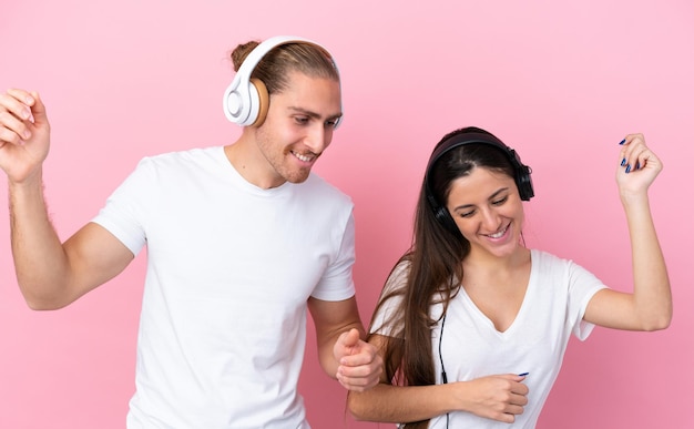 Jovem casal caucasiano isolado em fundo rosa ouvindo música e dançando