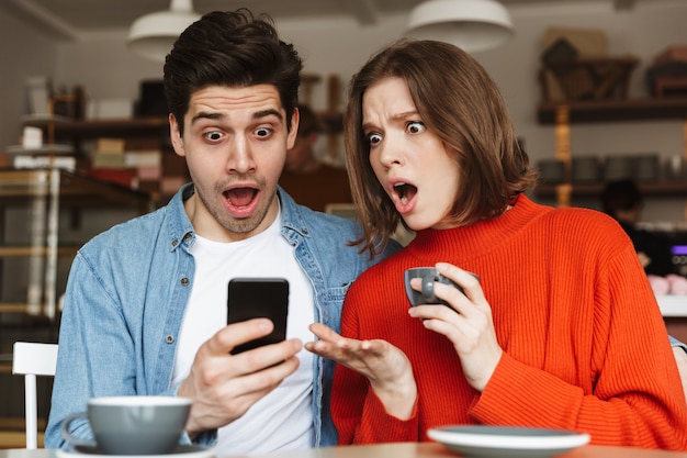 Jovem casal chocado sentado à mesa do café