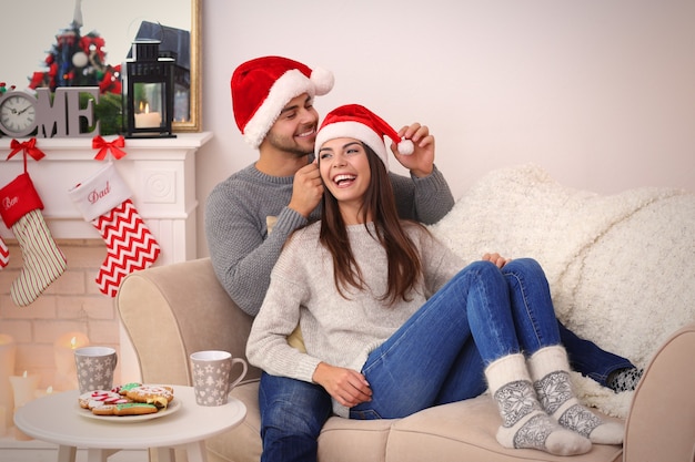 Jovem casal com chapéu de papai noel descansando em casa