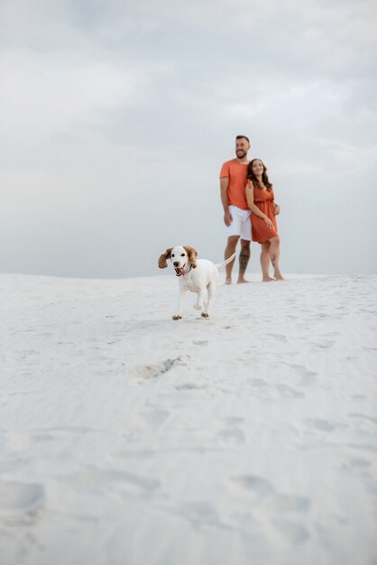 Jovem casal com roupas laranja com cachorro nas areias brancas do deserto