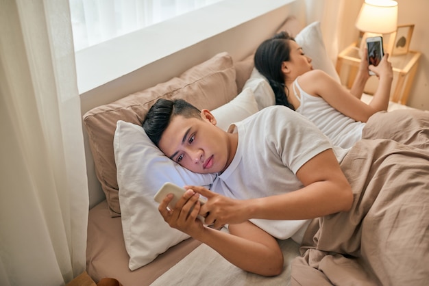 Jovem casal com smartphones na cama