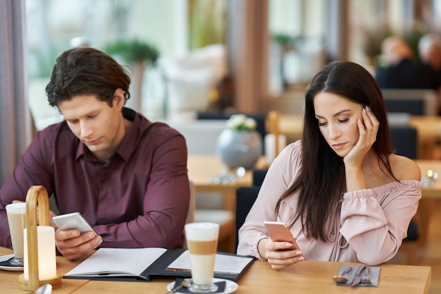 jovem casal com smartphones no café