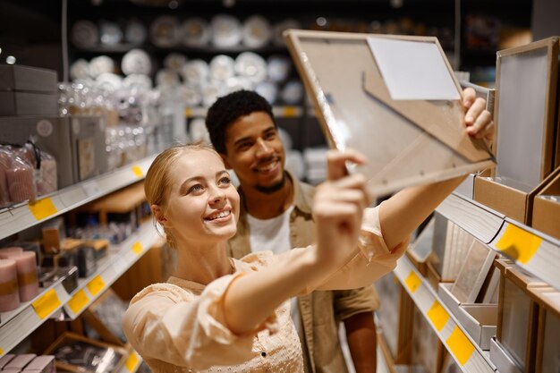 Jovem casal comprando porta-retrato na loja. Homem de mulher multiétnica escolhendo decoração para habitação