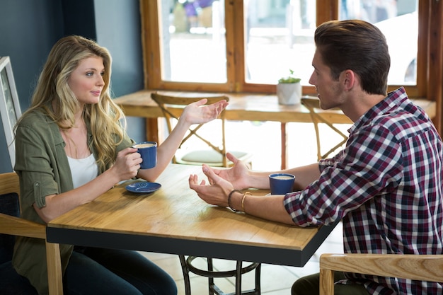 Jovem casal conversando enquanto toma um café na mesa de um café