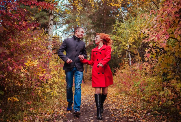 Jovem casal corre na floresta de outono entre árvores coloridas