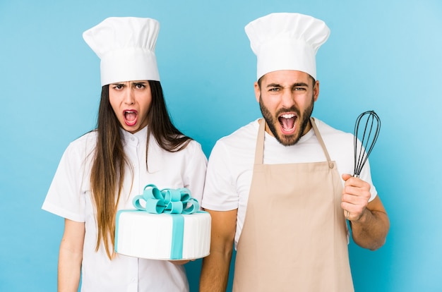 Jovem casal cozinhando um bolo juntos gritando muito irritado e agressivo.