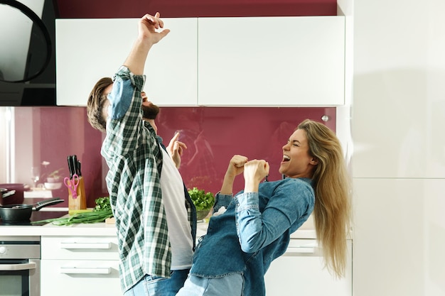 Jovem casal dançando na cozinha enquanto cozinha durante a manhã ensolarada