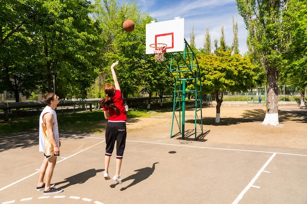 Jovem casal de atletas jogando basquete juntos - mulher dando um tiro na quadra ao ar livre do luxuriante parque verde