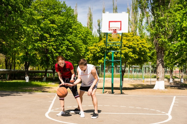 Jovem casal de atletas jogando basquete juntos na quadra ao ar livre no Parque Verdejante