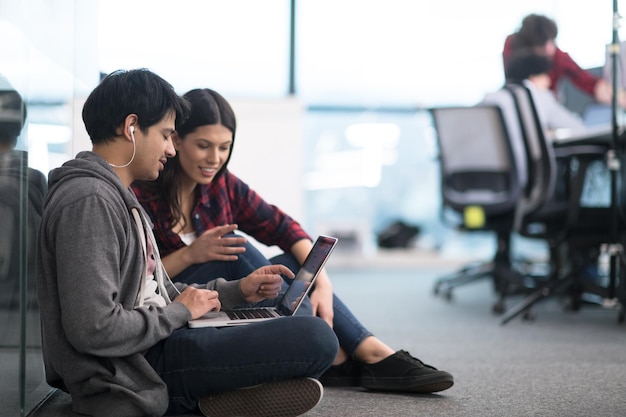 jovem casal de desenvolvedores de software usando laptop escrevendo código de programação enquanto está sentado no chão de um escritório de startups criativos modernos