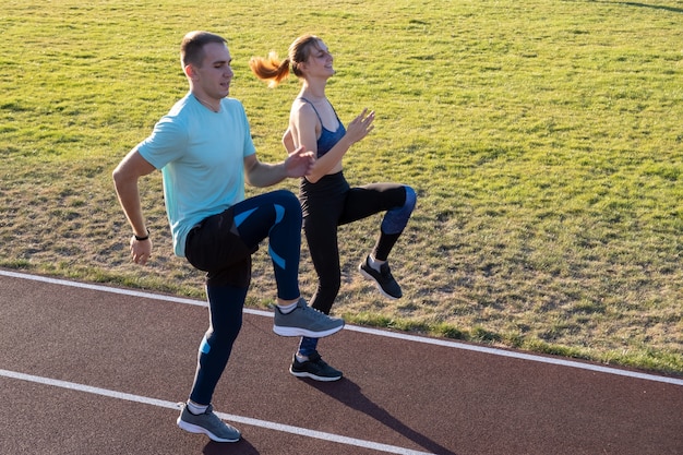 Jovem casal de desportistas em forma de menino e menina correndo ao fazer exercício em faixas vermelhas do estádio público ao ar livre.