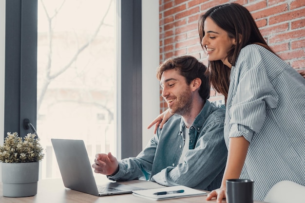 Jovem casal de família feliz rindo usando laptop olhando para a tela sentados à mesa sorrindo marido e mulher comprando escolhendo mercadorias on-line fazendo compras na internet pedidos com entrega em homexA