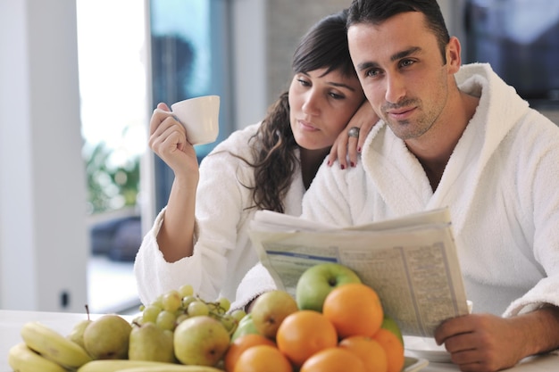 jovem casal de família lê jornal na cozinha de manhã com frutas frescas de café da manhã, comida e bebida de café na mesa