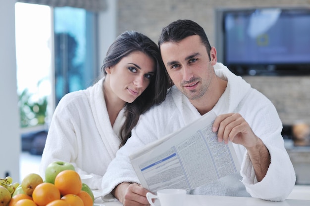 jovem casal de família lê jornal na cozinha de manhã com frutas frescas de café da manhã, comida e bebida de café na mesa