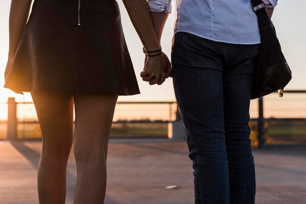 Foto jovem casal de mãos dadas no nível de estacionamento ao pôr do sol