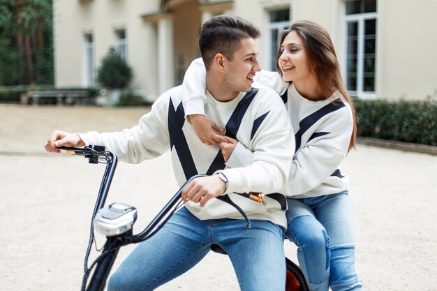 Jovem casal de namorados em roupas da moda anda de bicicleta