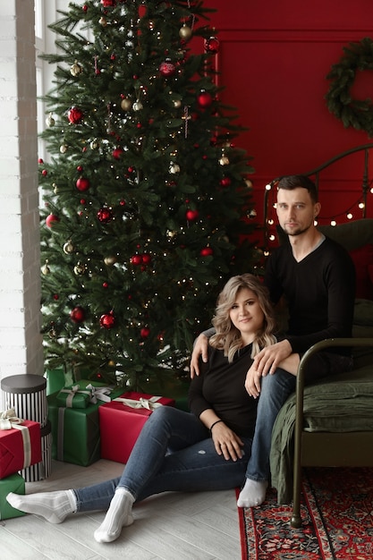 Jovem casal de namorados posando ao lado de uma árvore de Natal no interior decorado para o feriado de ano novo