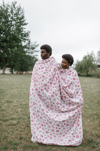 Jovem casal de pele escura embrulhado em folha juntos ao ar livre.