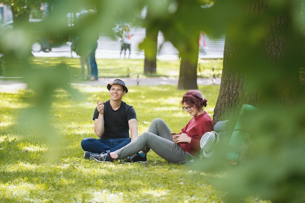 Jovem casal de turistas com mochilas descansando no parque, foto telefoto