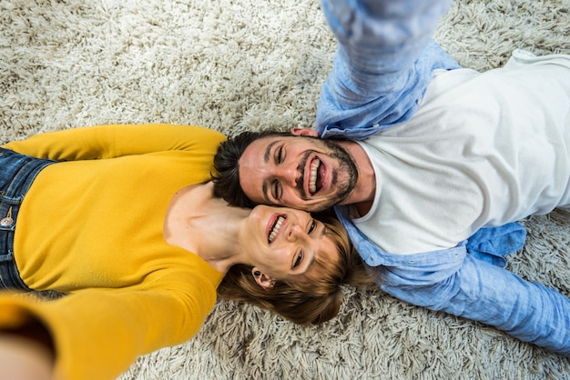 Jovem casal deitado no chão tirando uma selfie