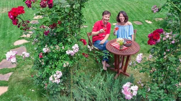 Jovem casal desfrutando de comida e vinho no belo jardim de rosas em encontro romântico, vista superior aérea de cima de homem e mulher comendo e bebendo juntos ao ar livre no parque