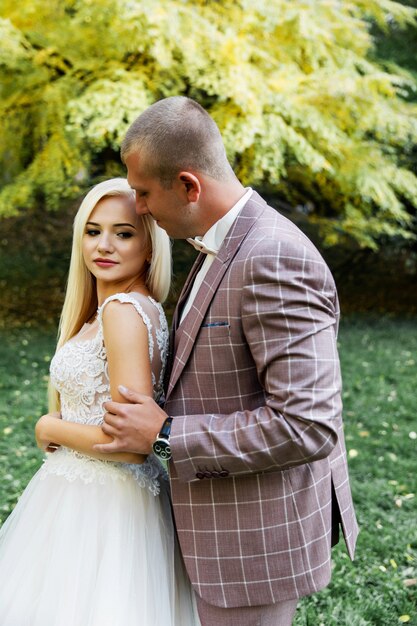 Jovem casal desfrutando de momentos românticos enquanto caminhava no parque. elegante noiva e noivo posando e beijando no parque no dia do casamento. noiva elegante em lindo vestido branco, noivo de terno.