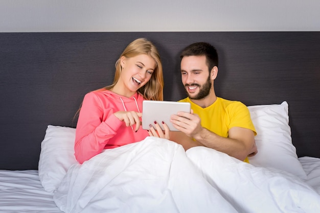 Jovem casal doce na cama assistindo algo no Tablet Gadget. Conceito sobre tecnologia e pessoas