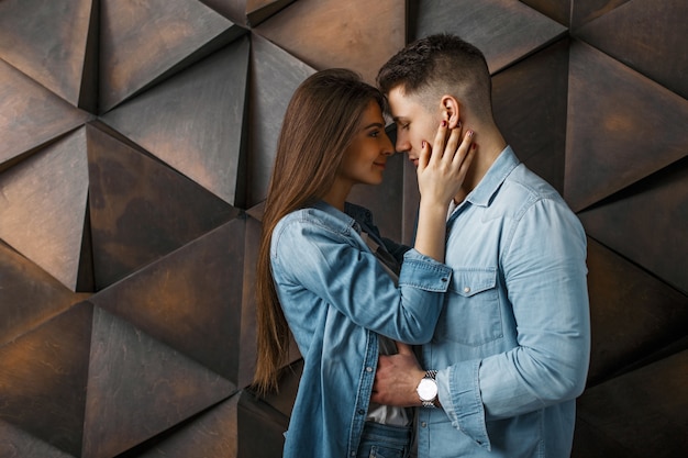 Jovem casal elegante com roupas jeans perto de uma parede de madeira vintage