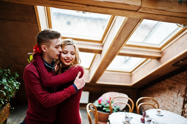 Jovem casal elegante lindo em um vestido vermelho em história de amor no café vintage com grandes janelas no telhado