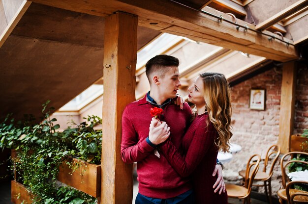 Jovem casal elegante lindo em um vestido vermelho em história de amor no café vintage com grandes janelas no telhado