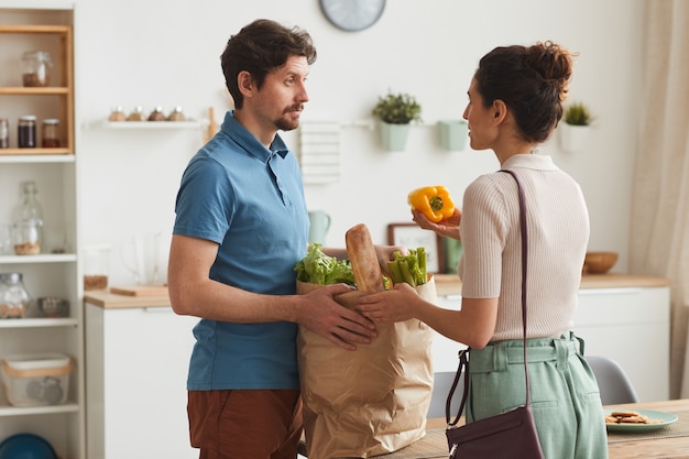 Jovem casal em pé na cozinha conversando enquanto tirava os legumes do saco de papel