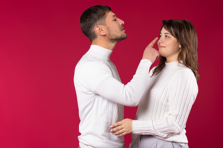 Foto jovem casal em suéteres brancos sobre um fundo vermelho. o homem toca o nariz da garota.