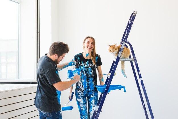 Jovem casal engraçado com gato fazendo renovação no apartamento novo.