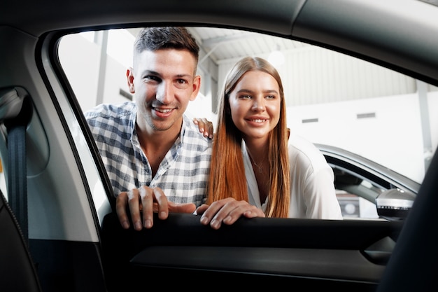 Jovem casal escolhendo o carro novo em uma loja de automóveis